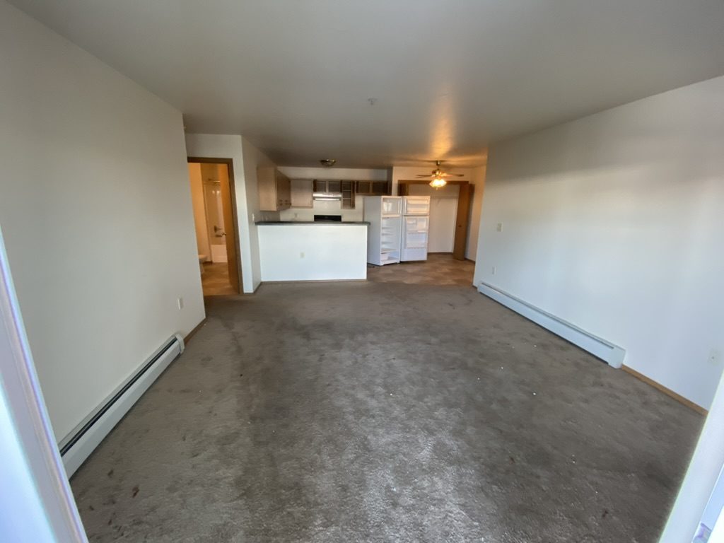 Empty living area with a kitchen visible in the background