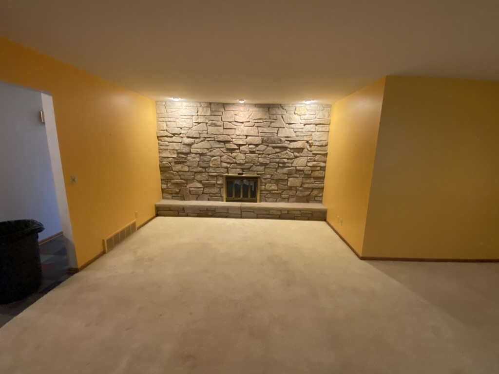 Empty basement room with a stone fireplace wall