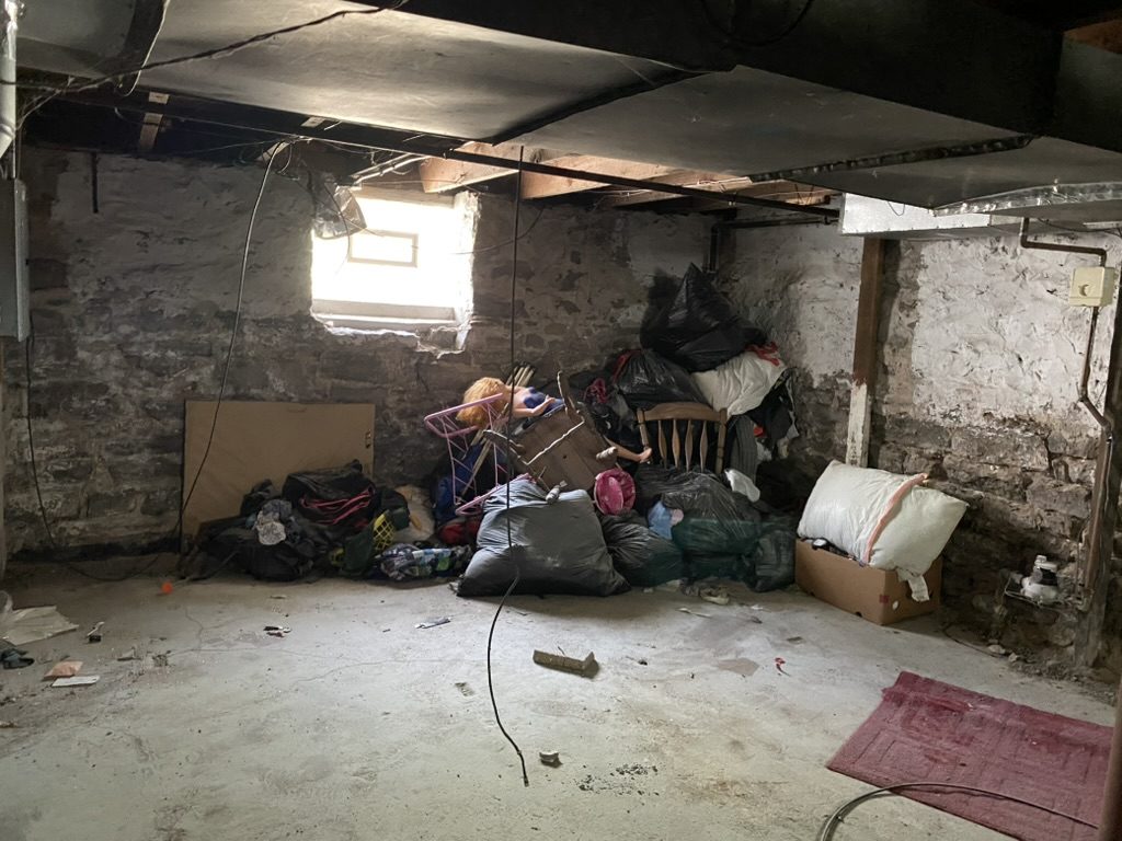 Basement with bags and loose items along a stone wall