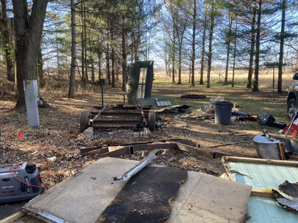 Dismantled material and loose outdoor items among trees.